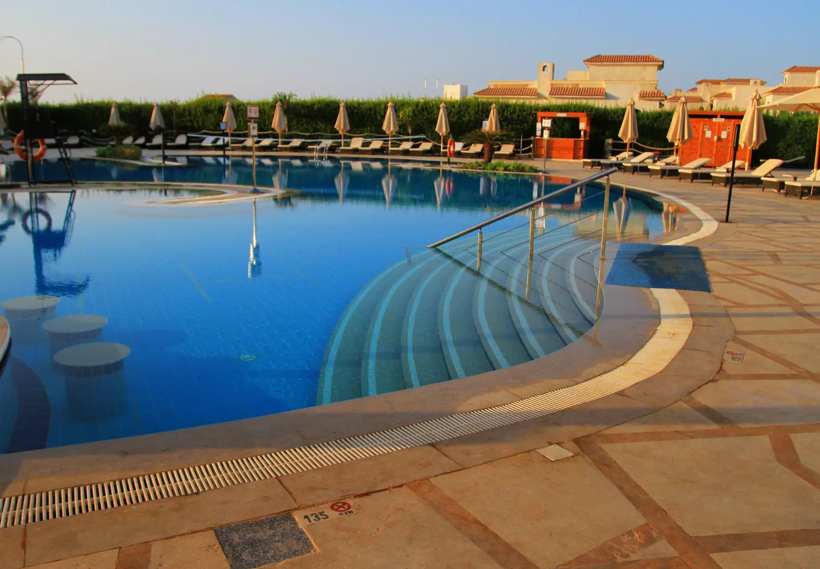 A resort pool with sun loungers under a clear sky